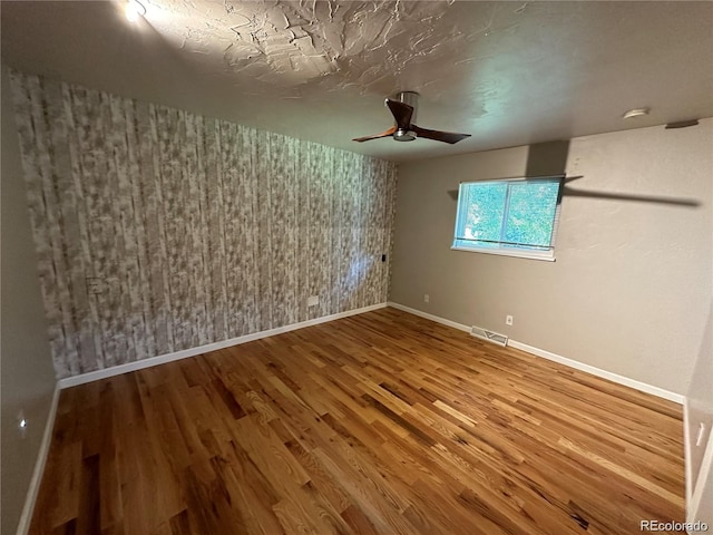 spare room with wood finished floors, visible vents, a ceiling fan, baseboards, and wallpapered walls