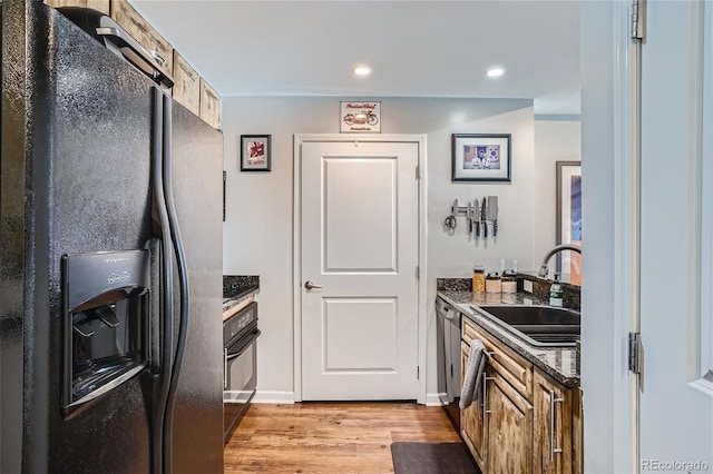 kitchen with sink, light hardwood / wood-style floors, dark stone counters, and black appliances