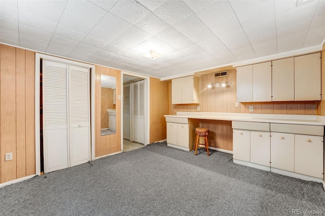 kitchen with light carpet, light countertops, cream cabinets, and wood walls