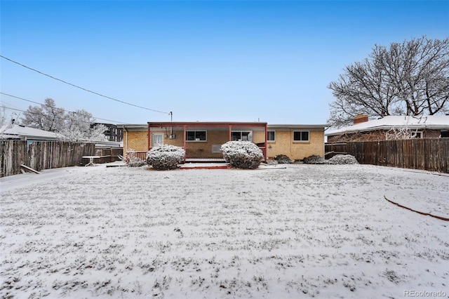 snow covered rear of property featuring fence and brick siding