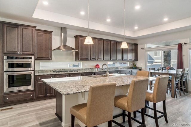 kitchen featuring a sink, stainless steel appliances, a raised ceiling, and wall chimney range hood