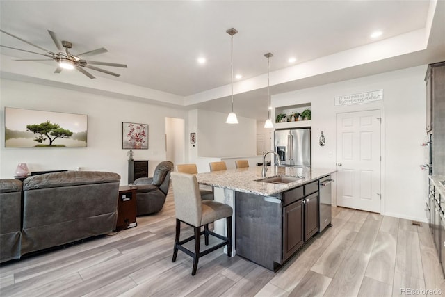 kitchen featuring a kitchen bar, a sink, open floor plan, appliances with stainless steel finishes, and light wood finished floors