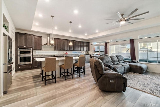 living room featuring recessed lighting, light wood-style flooring, a raised ceiling, and ceiling fan