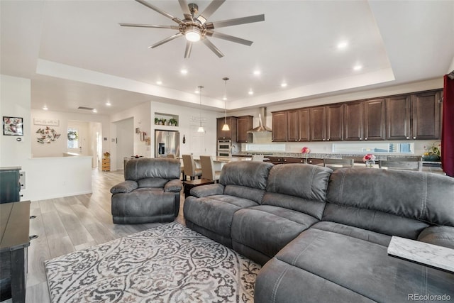 living room with light wood finished floors, recessed lighting, and a tray ceiling