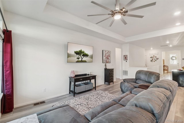 living room featuring visible vents, light wood-type flooring, a raised ceiling, and a ceiling fan