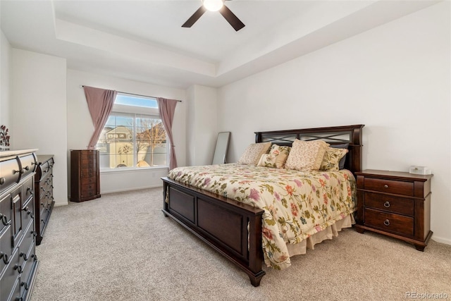 bedroom featuring light carpet, baseboards, a tray ceiling, and a ceiling fan