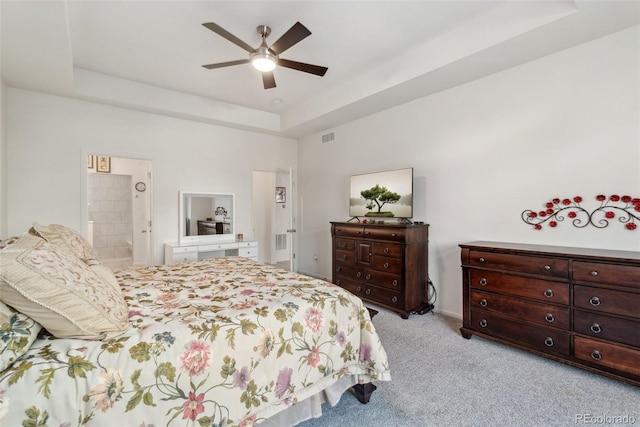 bedroom featuring visible vents, ensuite bath, a tray ceiling, ceiling fan, and light colored carpet