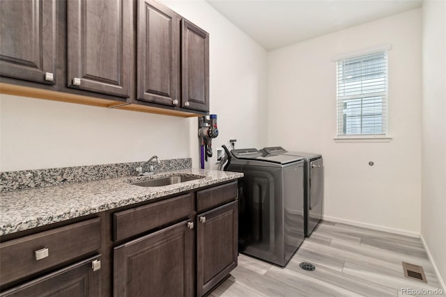 laundry room with visible vents, washing machine and clothes dryer, cabinet space, a sink, and light wood-style floors