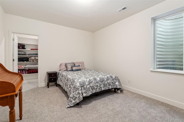 bedroom featuring visible vents, light carpet, baseboards, and a walk in closet