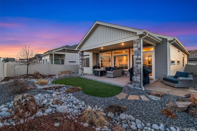 back of house at dusk with an outdoor living space, fence, and a patio area