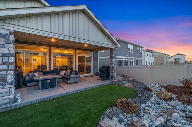 back of house at dusk with board and batten siding, an outdoor living space with a fire pit, fence, stone siding, and a patio