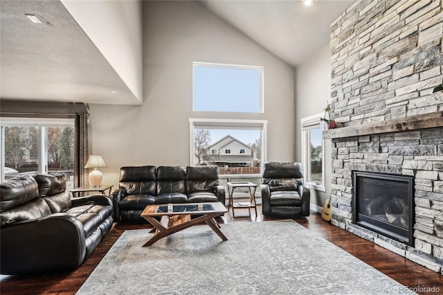 living area featuring high vaulted ceiling, dark wood-style floors, and a stone fireplace