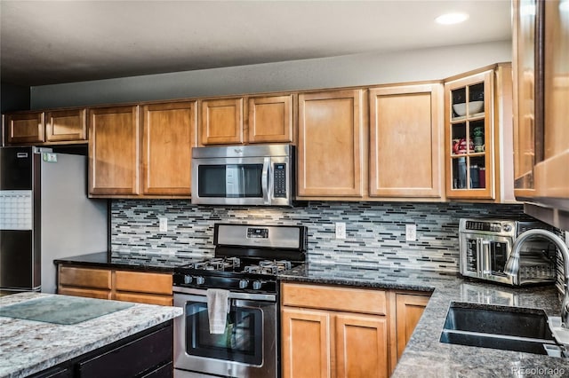 kitchen featuring dark stone counters, appliances with stainless steel finishes, glass insert cabinets, and a sink