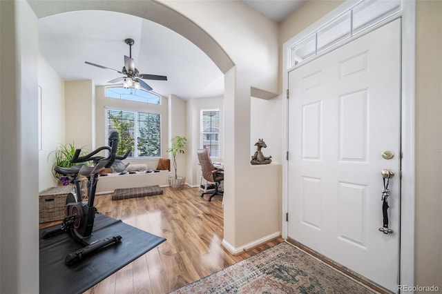 exercise room with baseboards, lofted ceiling, light wood-style floors, arched walkways, and a ceiling fan
