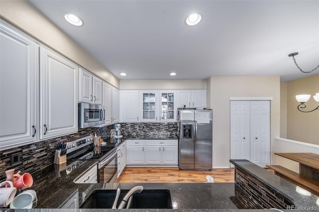 kitchen featuring a sink, tasteful backsplash, stainless steel appliances, dark stone counters, and glass insert cabinets