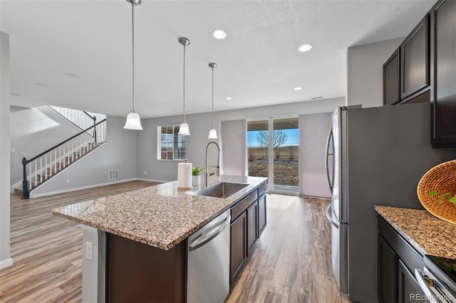 kitchen featuring dark brown cabinetry, sink, stainless steel appliances, pendant lighting, and a kitchen island with sink