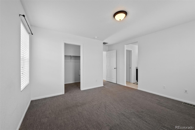 unfurnished bedroom featuring dark carpet, a walk in closet, and a closet