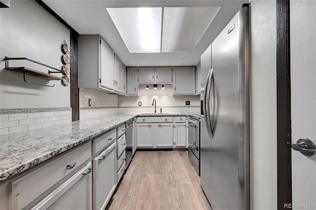 kitchen with stainless steel appliances, sink, backsplash, and light hardwood / wood-style flooring