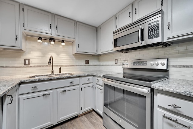 kitchen with sink, light hardwood / wood-style flooring, appliances with stainless steel finishes, tasteful backsplash, and light stone counters