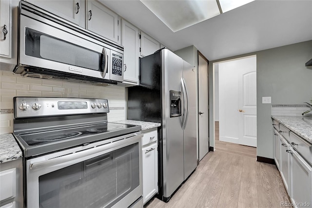 kitchen featuring white cabinetry, tasteful backsplash, light hardwood / wood-style flooring, appliances with stainless steel finishes, and light stone countertops