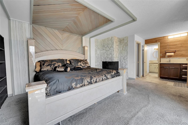 carpeted bedroom featuring a stone fireplace, a textured ceiling, wooden walls, and ensuite bath