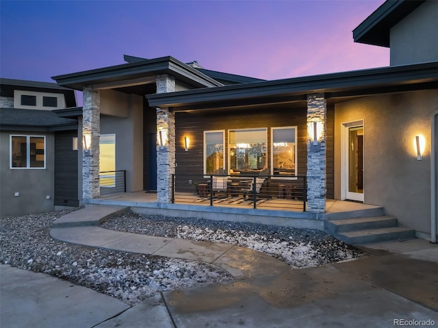 exterior entry at dusk with stucco siding and covered porch