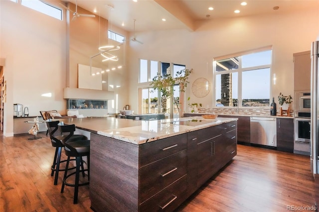 kitchen with modern cabinets, a kitchen breakfast bar, stainless steel appliances, a towering ceiling, and dark wood-style flooring