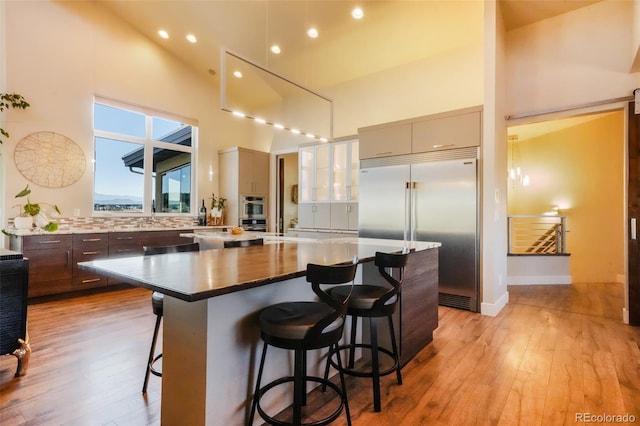 kitchen featuring a breakfast bar, light wood-style flooring, built in refrigerator, and a towering ceiling