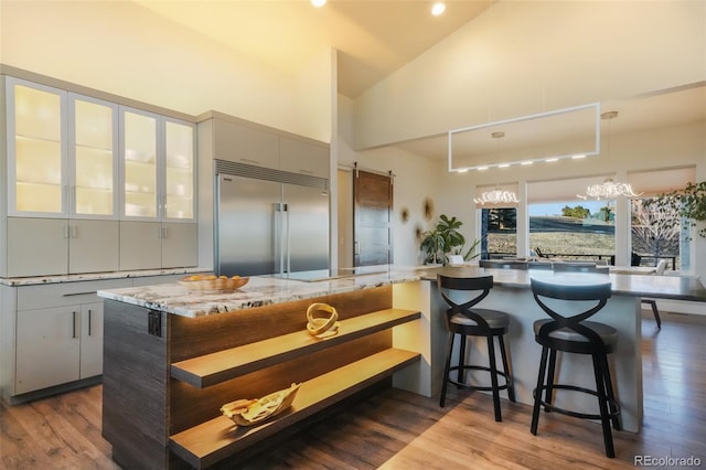 kitchen featuring built in refrigerator, high vaulted ceiling, dark wood-type flooring, a kitchen breakfast bar, and a spacious island