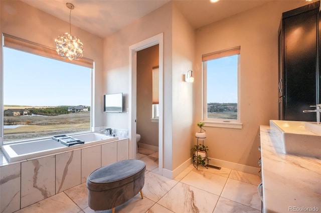 bathroom with baseboards, a chandelier, toilet, a garden tub, and a sink