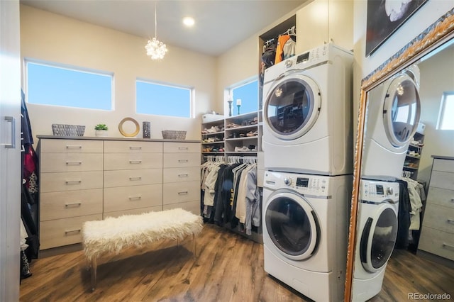 laundry room featuring laundry area, a notable chandelier, wood finished floors, and stacked washing maching and dryer