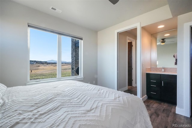 bedroom with dark wood-style floors, visible vents, baseboards, ensuite bath, and recessed lighting