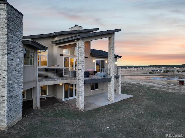 back of property featuring stucco siding, a water view, a chimney, and a patio area