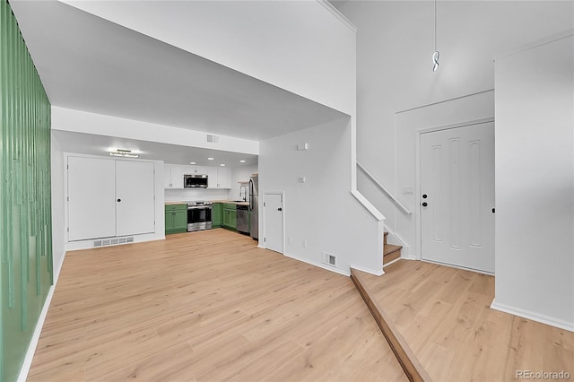 unfurnished living room featuring light wood-type flooring, visible vents, baseboards, and stairs