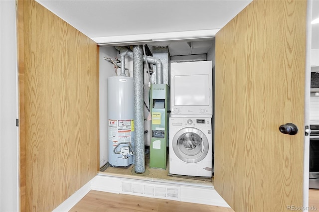 washroom featuring water heater, stacked washer / drying machine, laundry area, and wood finished floors