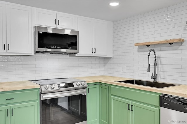 kitchen with green cabinetry, butcher block counters, appliances with stainless steel finishes, and a sink