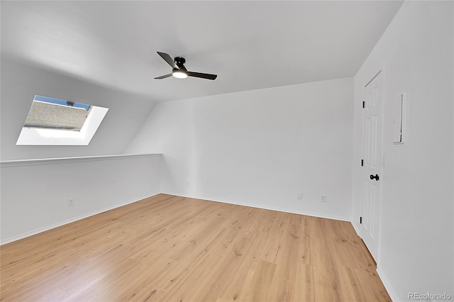 spare room with light wood-type flooring, lofted ceiling with skylight, baseboards, and ceiling fan