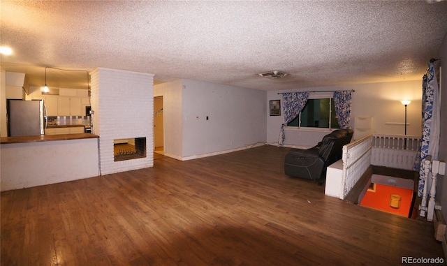 unfurnished living room featuring hardwood / wood-style floors, a textured ceiling, and a brick fireplace