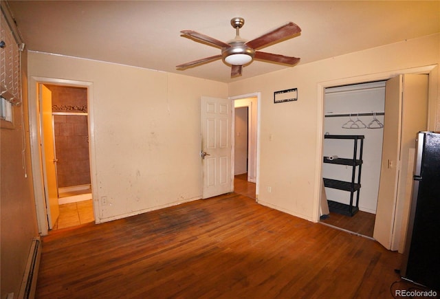 unfurnished bedroom with baseboard heating, dark wood-type flooring, stainless steel fridge, connected bathroom, and a closet