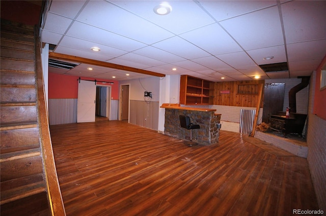 unfurnished living room featuring a barn door, a paneled ceiling, indoor bar, and hardwood / wood-style floors