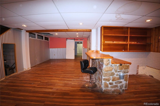 unfurnished living room featuring built in shelves, a drop ceiling, a barn door, and dark hardwood / wood-style floors