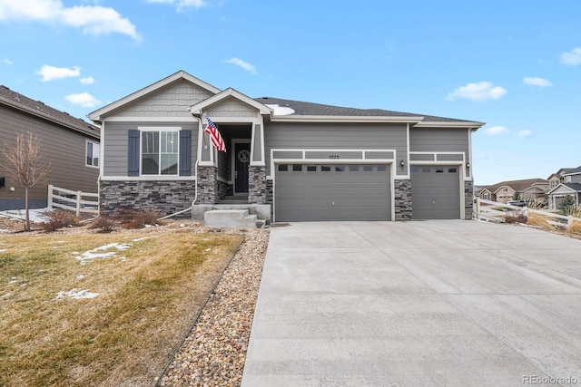 craftsman inspired home with a garage, stone siding, driveway, and fence