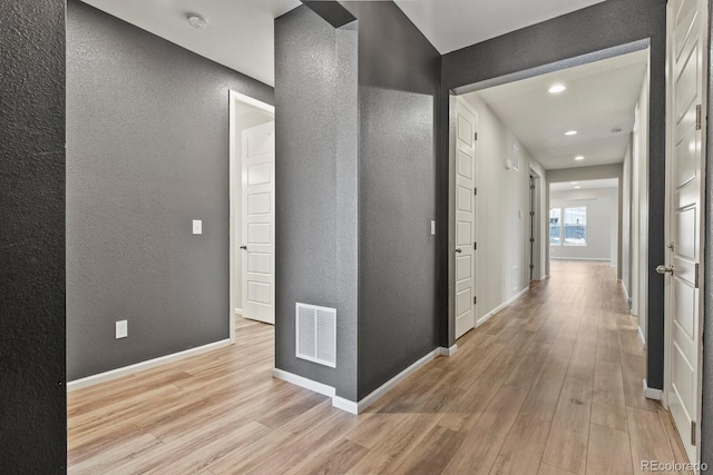 corridor featuring baseboards, visible vents, a textured wall, and light wood finished floors