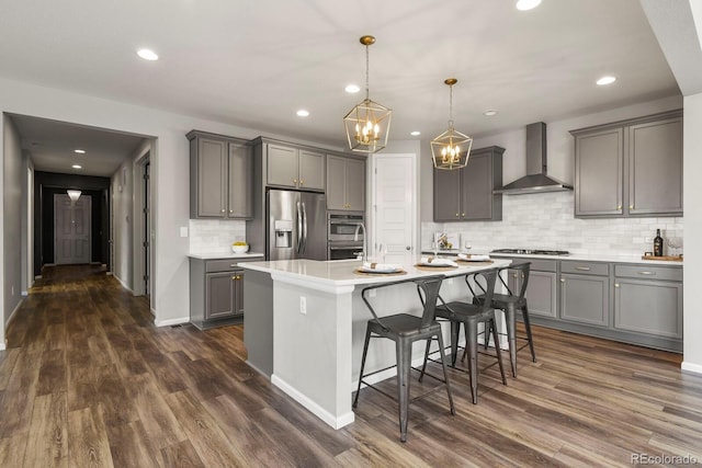 kitchen with dark wood finished floors, wall chimney exhaust hood, appliances with stainless steel finishes, a breakfast bar, and gray cabinets