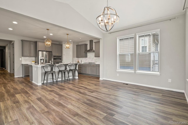 kitchen with lofted ceiling, a notable chandelier, gray cabinetry, appliances with stainless steel finishes, and wall chimney range hood