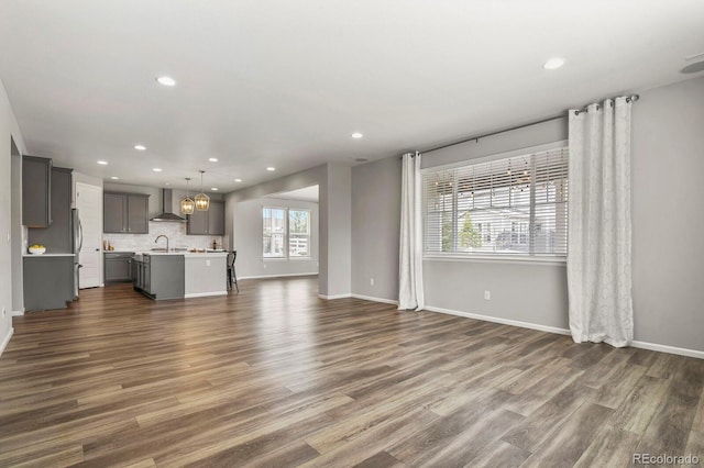 unfurnished living room with dark wood-style floors, recessed lighting, a sink, and baseboards