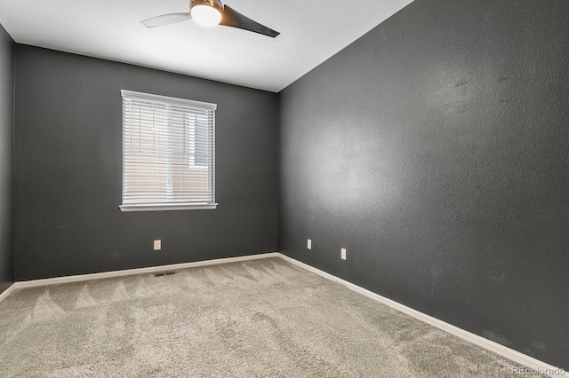 carpeted spare room featuring visible vents, a textured wall, a ceiling fan, and baseboards