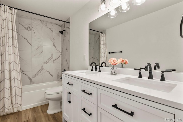 full bathroom with double vanity, a sink, toilet, and wood finished floors