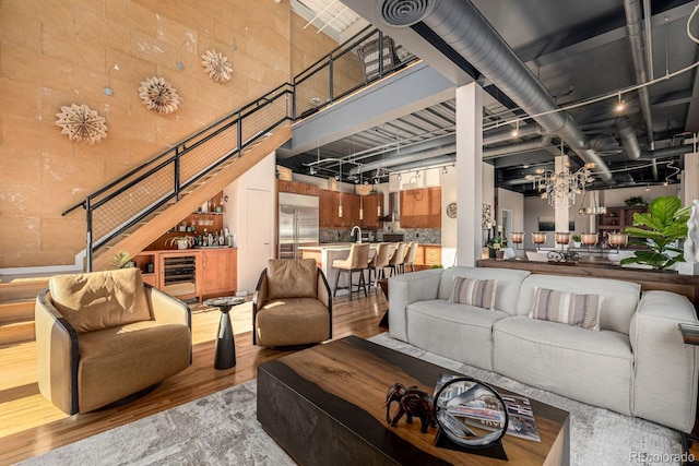 living area featuring a towering ceiling, beverage cooler, a chandelier, and wood finished floors