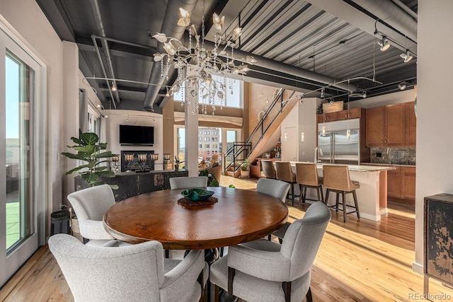 dining room with track lighting, a multi sided fireplace, light wood finished floors, and stairs